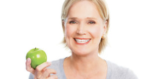 middle aged blonde woman green apple and smiling